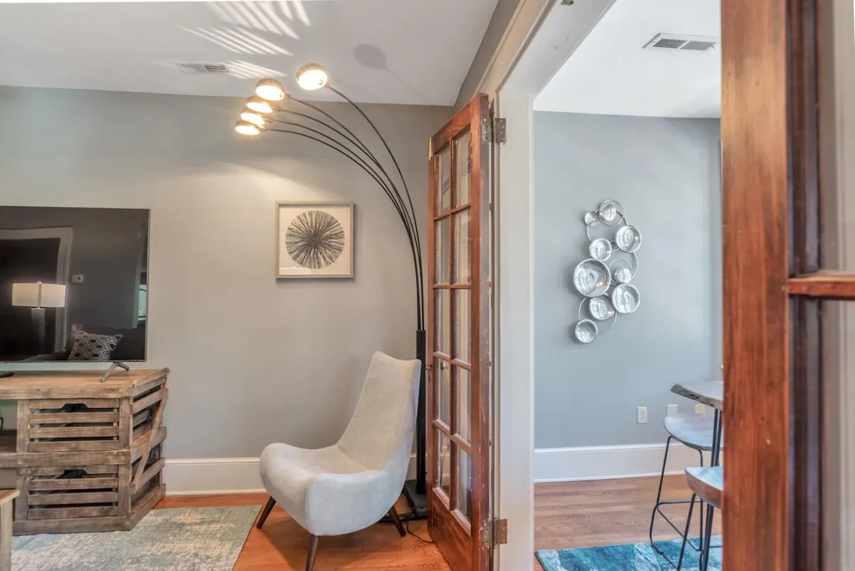The hero image showcases a stylish, sunlit living area with a modern arc floor lamp, a unique wooden crate coffee table, contemporary seating, and curated wall art including decorative glass plates. The space feels cozy yet sophisticated, blending historic character with modern comfort—an inviting spot for reading, socializing, or simply relaxing.