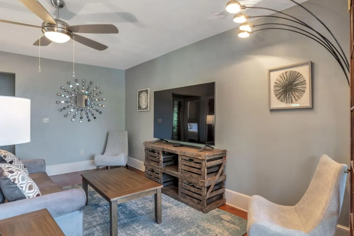 This casual and comfortable space highlights a mirror with a decorative arrangement, a wooden coffee table, a TV unit constructed of crates, and cozy seating. The layout suggests a hallway or entry-adjacent living area, offering a glimpse of the welcoming atmosphere as you enter the home.