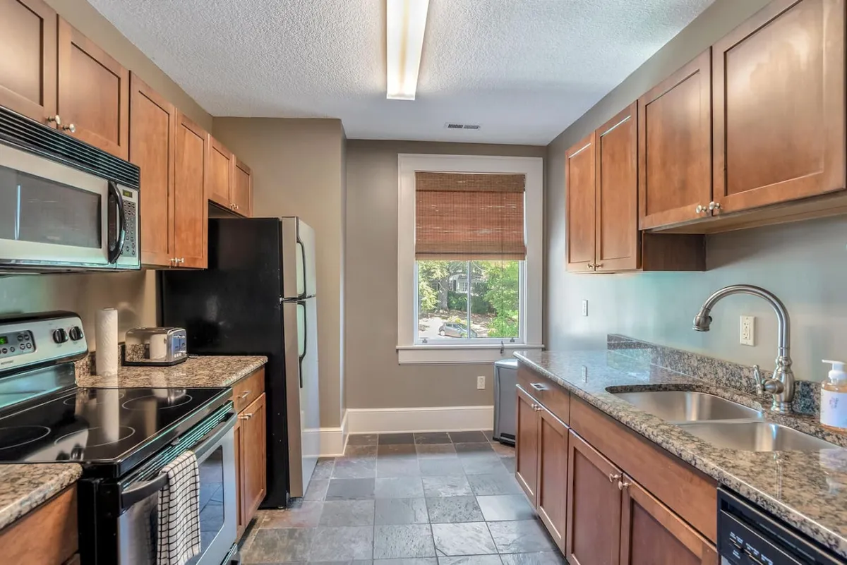A warm, inviting kitchen space featuring sleek granite countertops and state-of-the-art stainless steel appliances. Sunlight filters through a window, illuminating the modern design and providing a cheerful, cozy mood. The layout hints at ample workspace for both cooking elaborate meals and preparing snacks. Subtle details suggest the space is perfect for entertaining or enjoying quiet mornings over coffee.