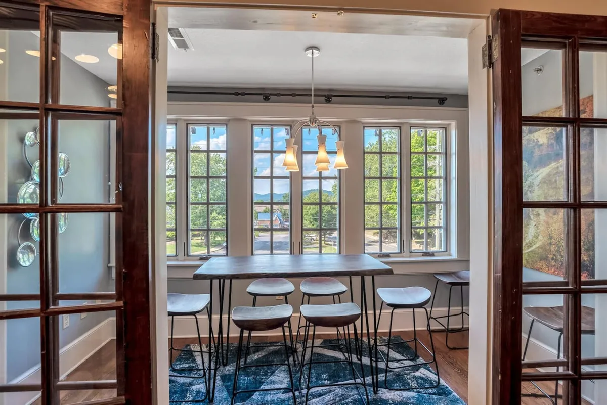 A stylish dining area is depicted, featuring a modern table set beneath attractive light fixtures and flanked by windows that invite in daylight and city views. The room is ready for gathering, welcoming guests into a bright, functional entry and dining space.